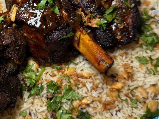 Nihari Lamb Shank served over Chickpea Rice in a blue ceramic platter, garnished with fresh parsley, caramelized onions, and nihari gravy, made with Royal Basmati Rice