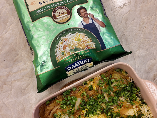 Vegetable Paneer Biryani garnished with caramelized onions and fresh cilantro in a baking dish, alongside Daawat Ultima Basmati Rice