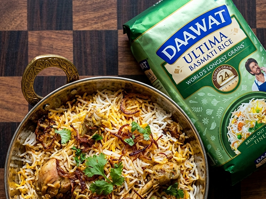 Chicken Dum Biryani garnished with fried onions and fresh cilantro in a brass kadai, alongside Daawat Ultima Basmati Rice
